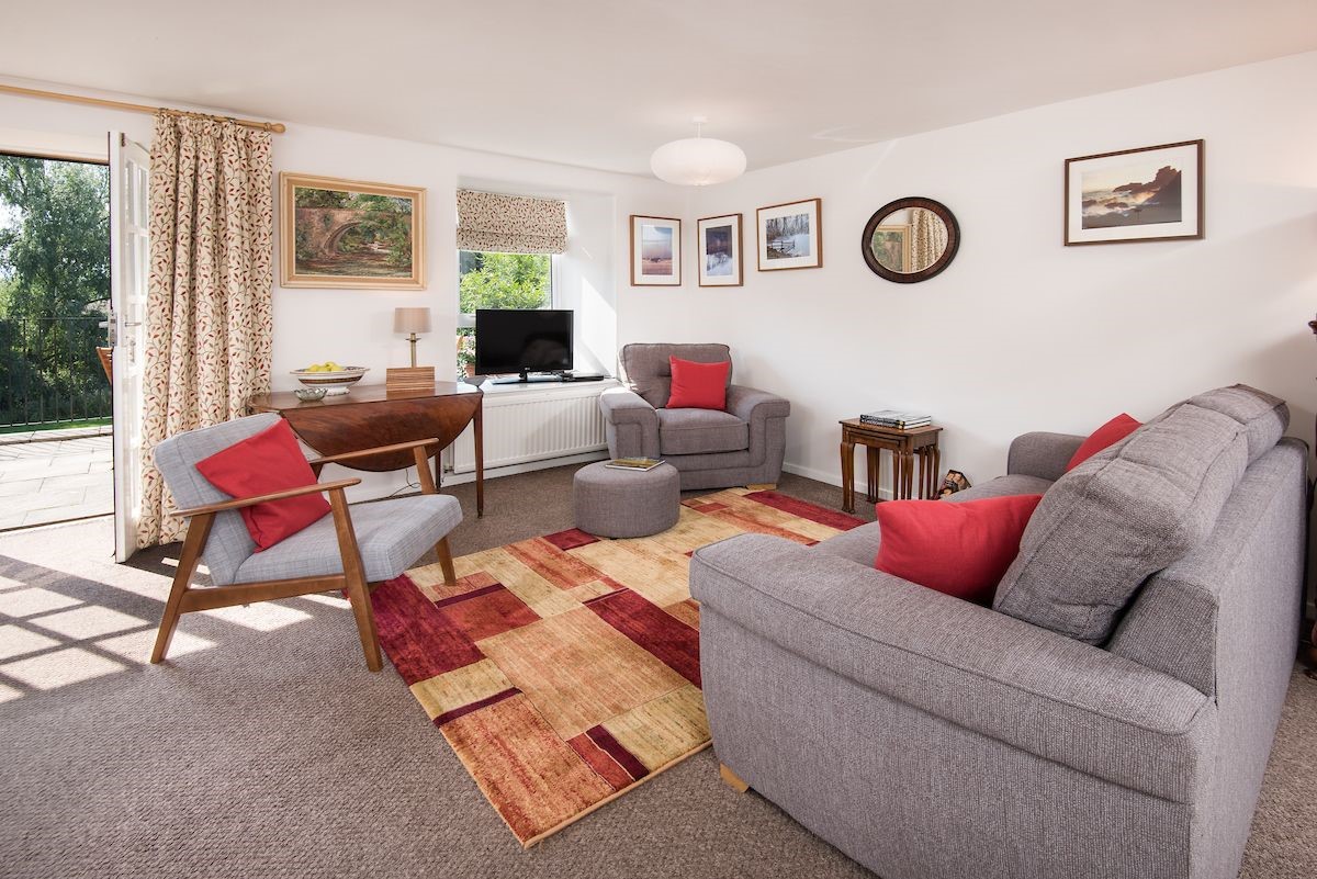 Coldstream Coach House - sitting room with sofa, TV, two armchairs and door leading to the patio