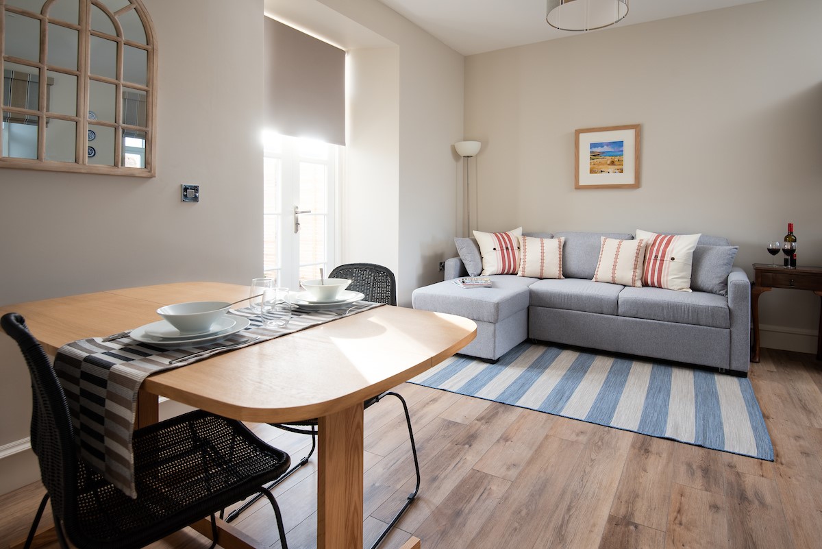 Cambridge House Cottage Number One - the open-plan living area with corner sofa and dining table seating two guests