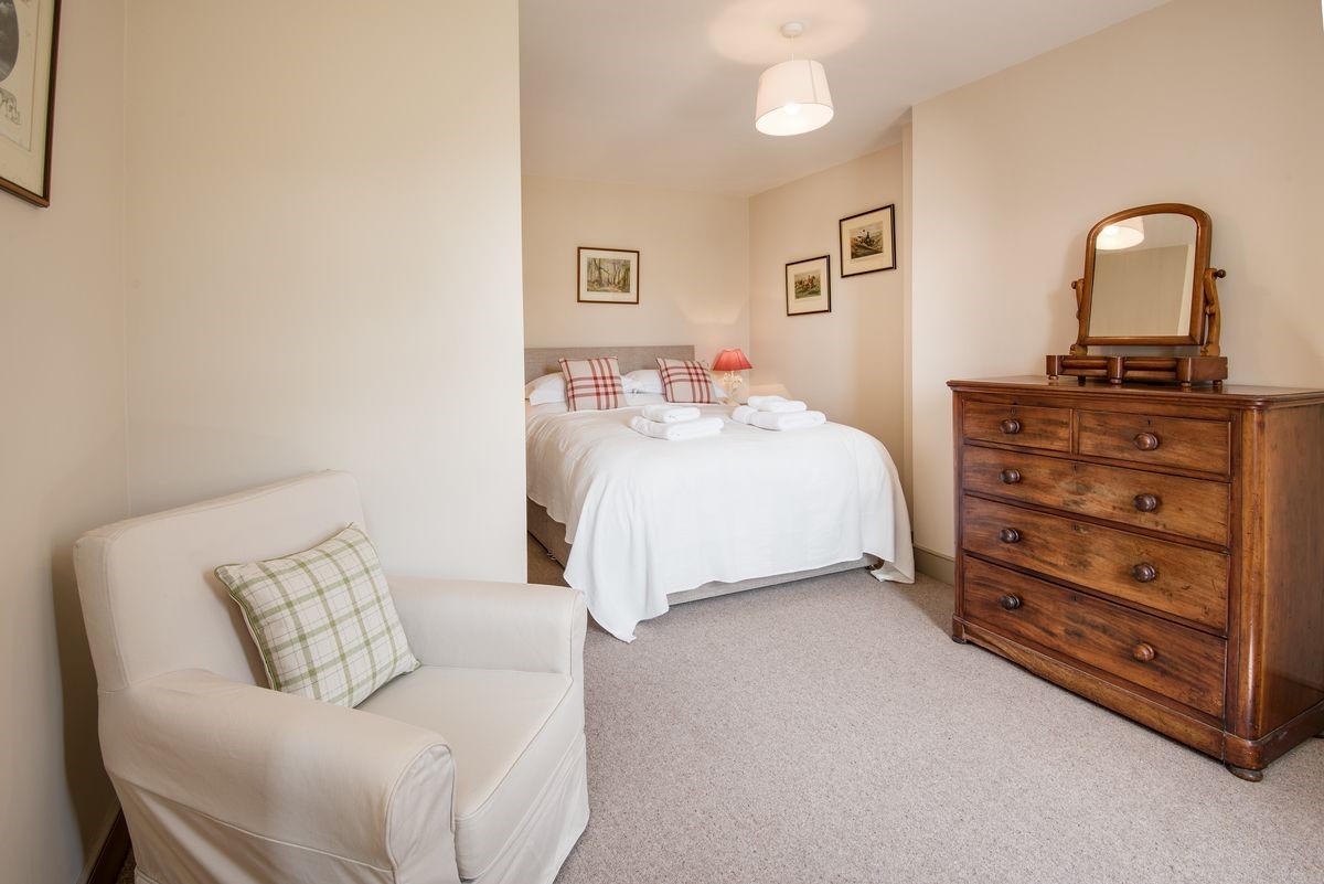 College Cottage - bedroom one on the ground floor with king size bed, chest of drawers and armchair
