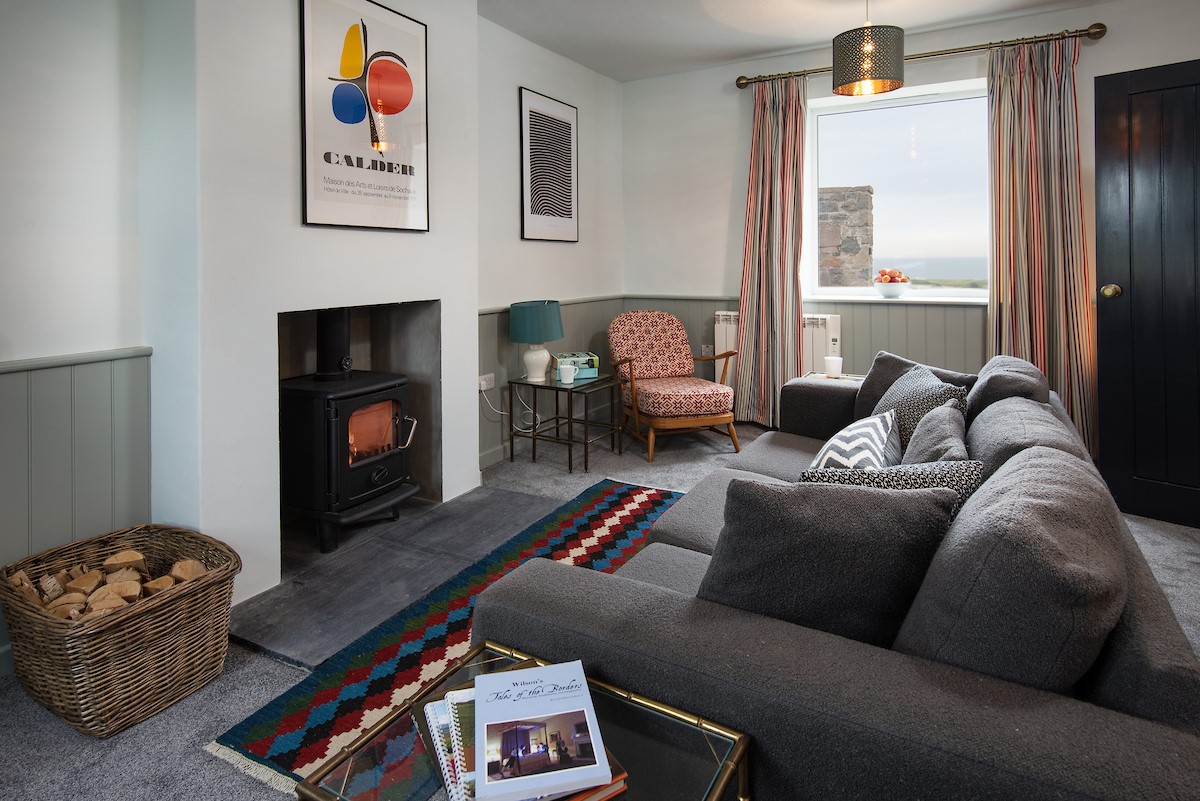Calder Cottage - sitting room with wood burning stove, sofa, armchair and sea views