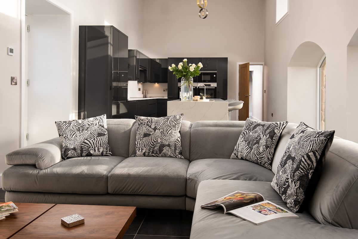 The Steading at West Lyham - sitting room with corner sofa and statement cushions leading to monochrome kitchen