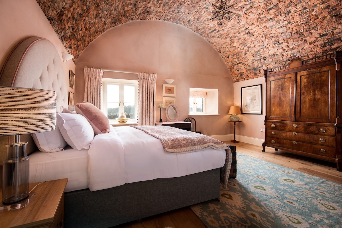 Lakeside Cottage - Alice - bedroom one boasts exposed brick arched ceilings and a tasteful blush pink colour scheme