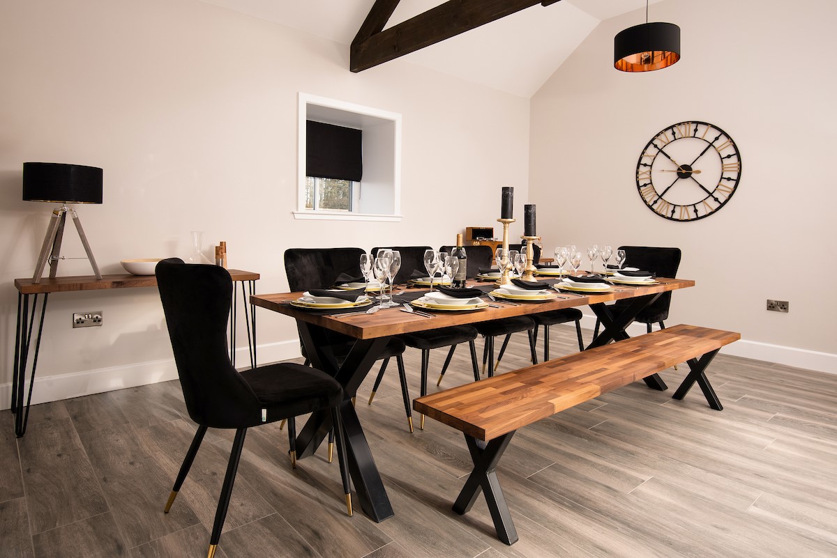 The Steading at West Lyham - stylish dining area with large table, six chairs and bench seat with black and copper details
