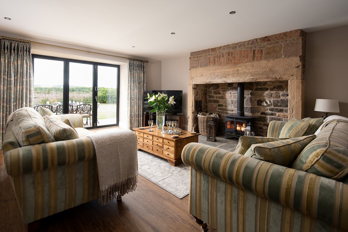 Brockmill Farmhouse - sitting room with large comfortable sofas, wood-burning stove and patio doors