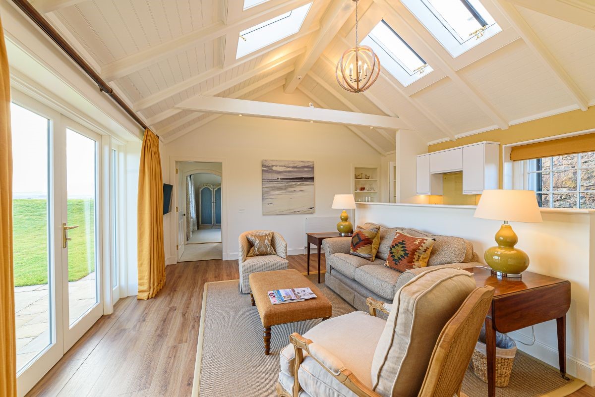 Fenton Lodge - open-plan living area with double height ceiling, French doors leading outside, sofa and two armchairs