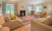 Gardener's Cottage - spacious sitting room with two sofas, armchairs, wood burning stove and French doors