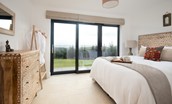 The Elm - bedroom with kingsize bed, chest of drawers with mirror above, open clothes rail and door out to outdoor patio area